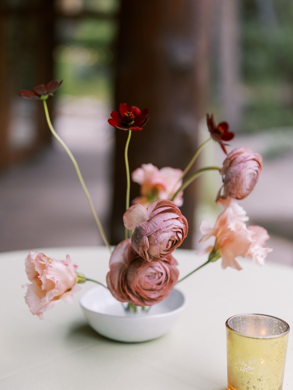 Delicate pink and red garden roses arranged in elegant white vessels against a neutral background.