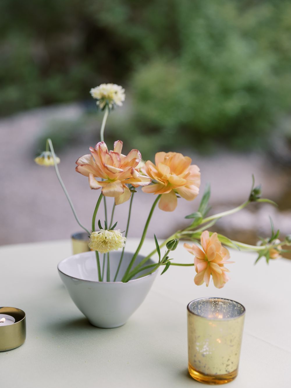 Peach roses and white flowers arranged in a small white bowl with gold mercury glass accents.