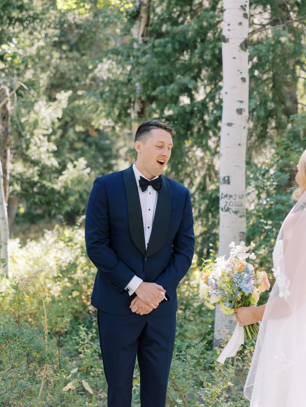 A couple shares a joyful first look moment in a sunlit aspen grove during their wedding day.