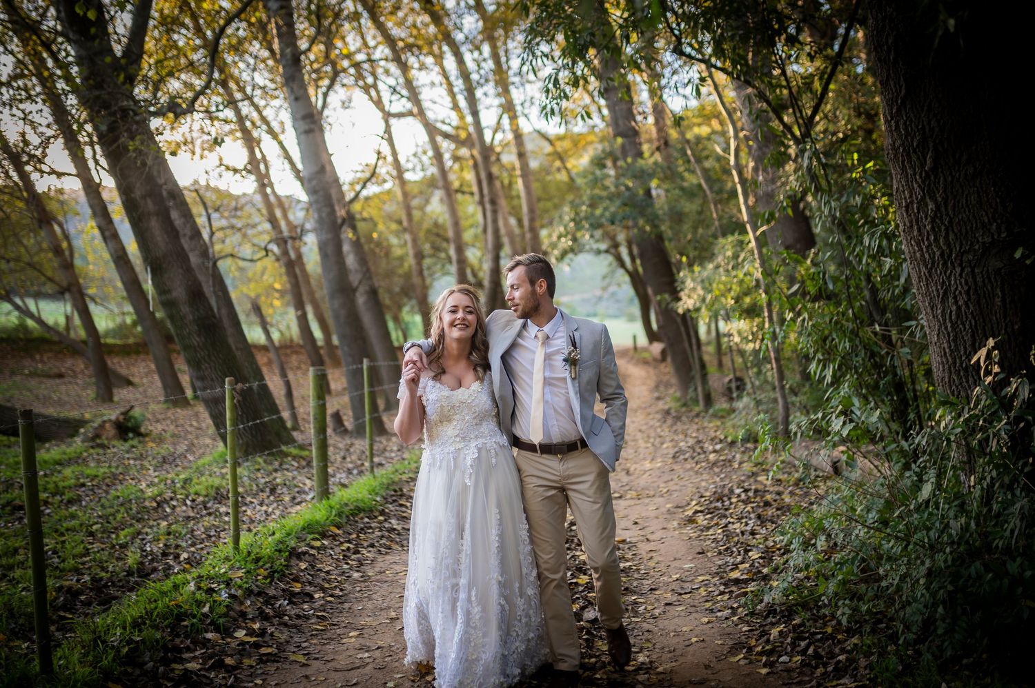 A couple enjoys a romantic forest setting at sunset as they stand together on a wooded path.