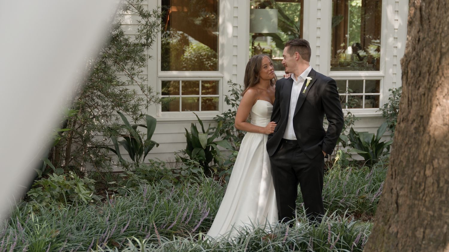 A bride and groom share an intimate moment together in a garden setting with white columns and trees.