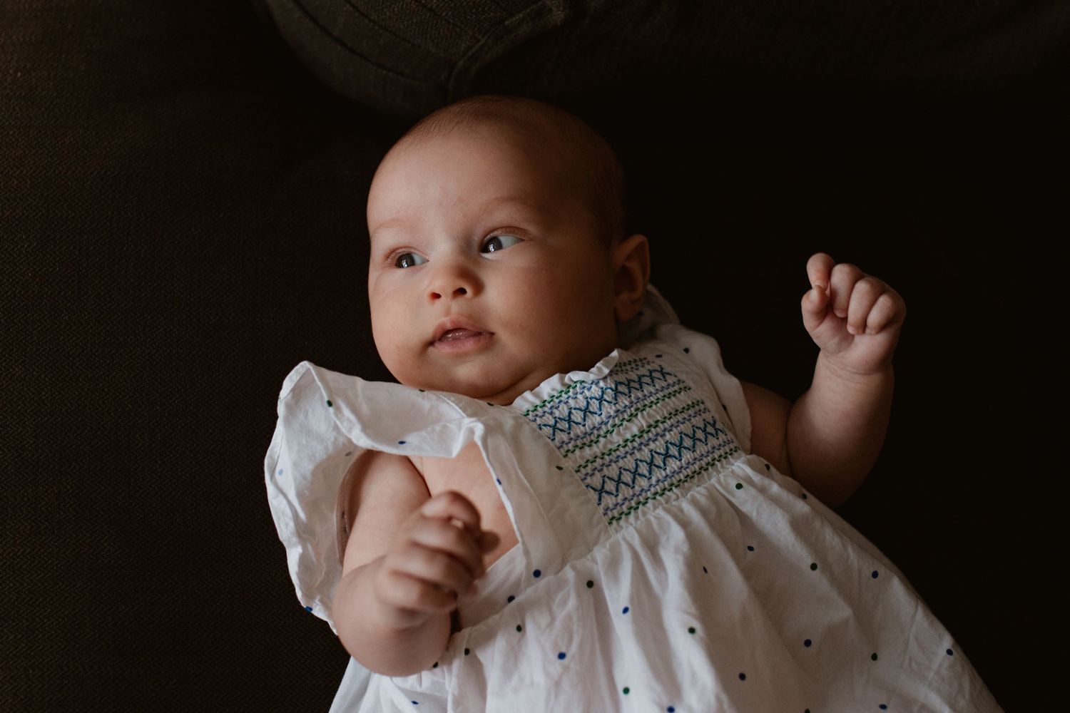 Close-up portrait of a baby in white clothing against a dark background.