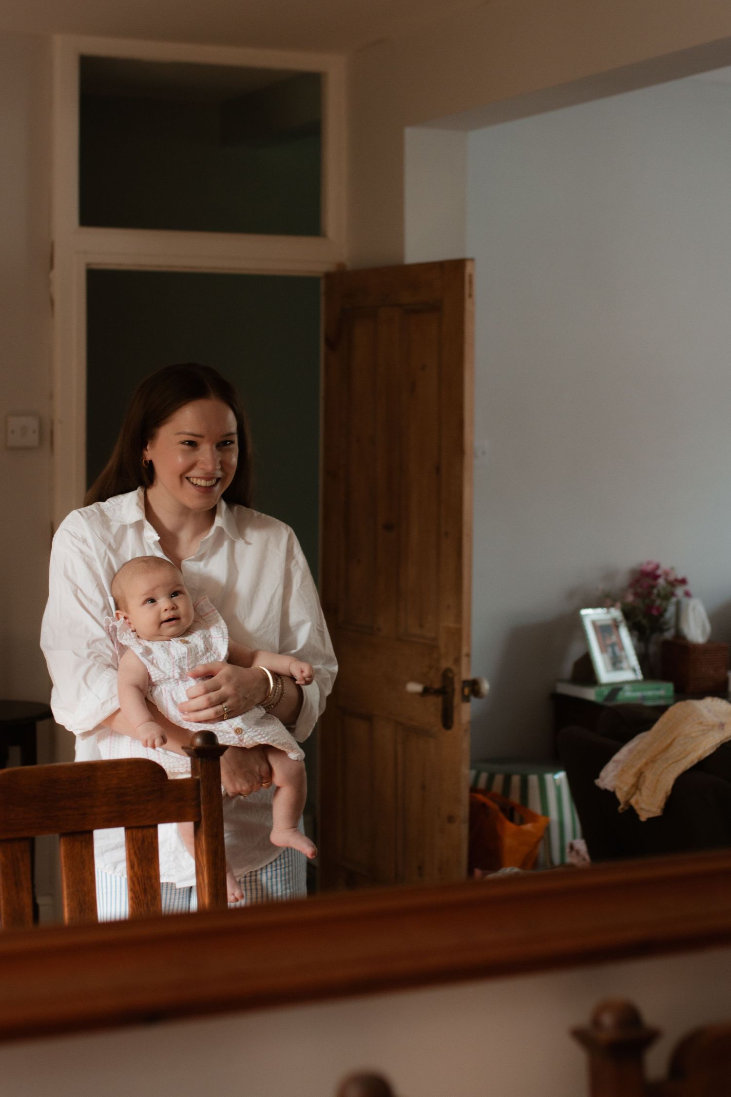 Parent and baby reflected in a wooden-framed mirror while standing in a cozy room.