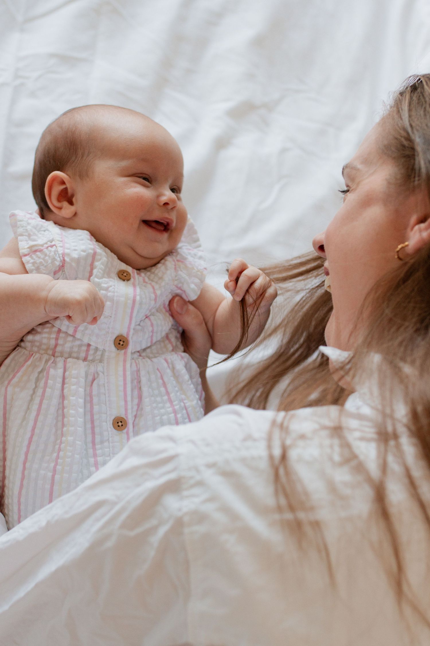 Intimate lifestyle portraits of parent and baby lying together on white bedding.