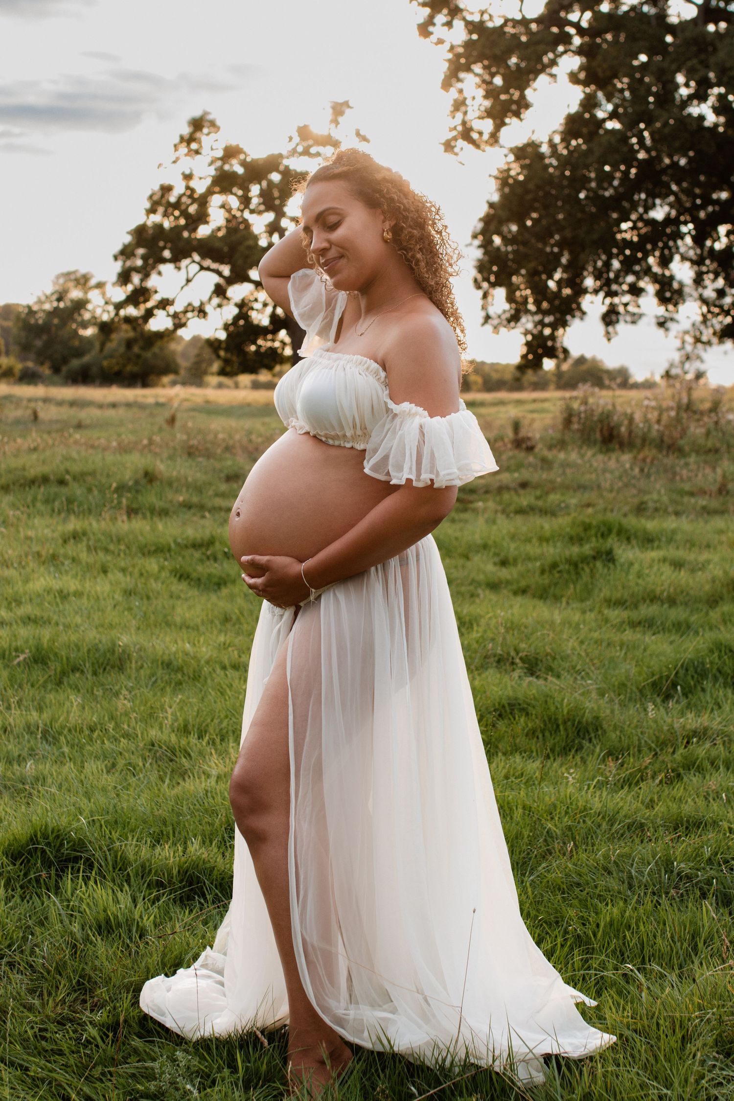 Maternity photos in flowing white dress taken at sunset in grassy field.
