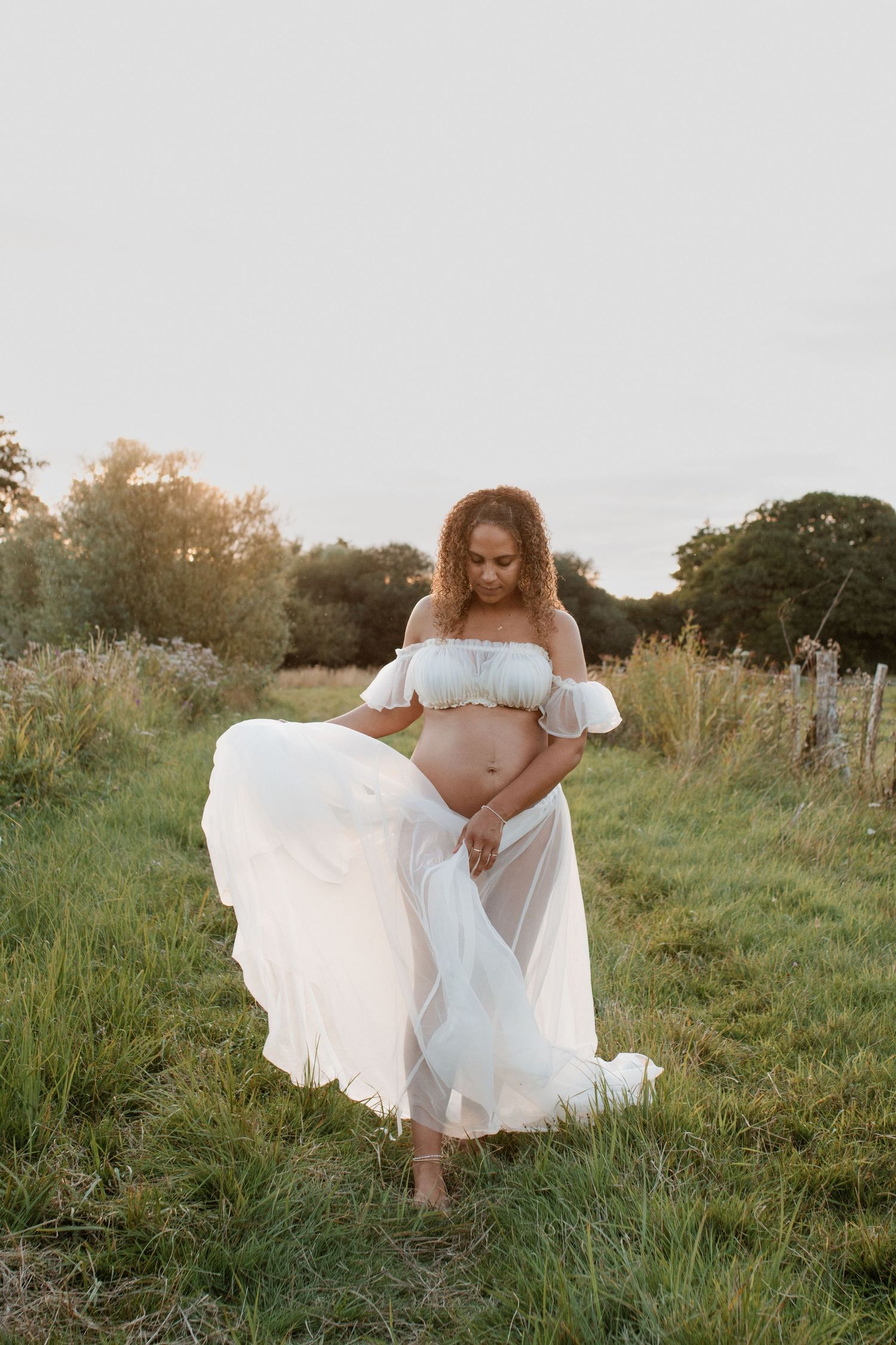 Ethereal maternity portraits showing flowing white dress movement in outdoor field setting.