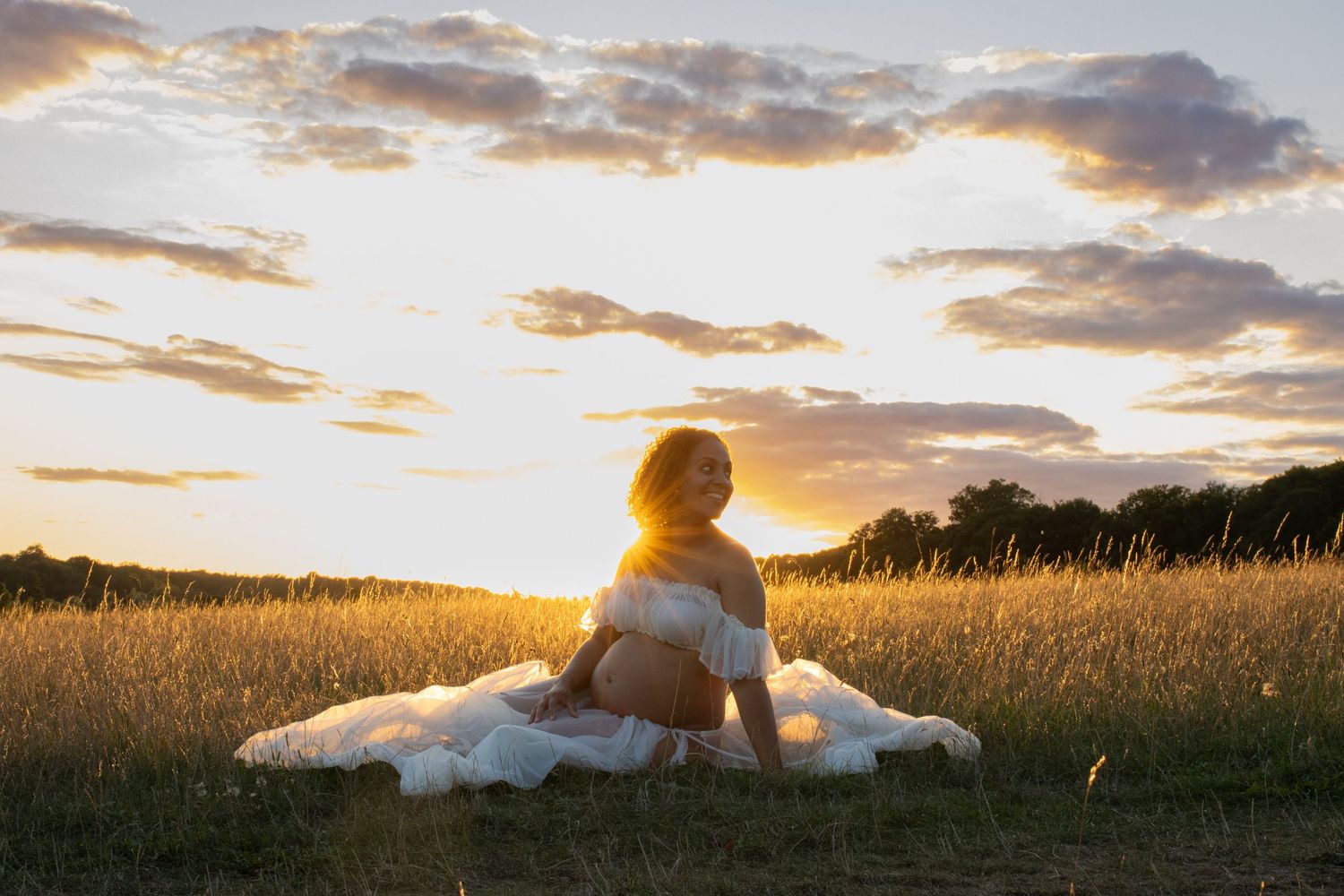 Silhouette of a person in a flowing dress sitting in a golden field at sunset.