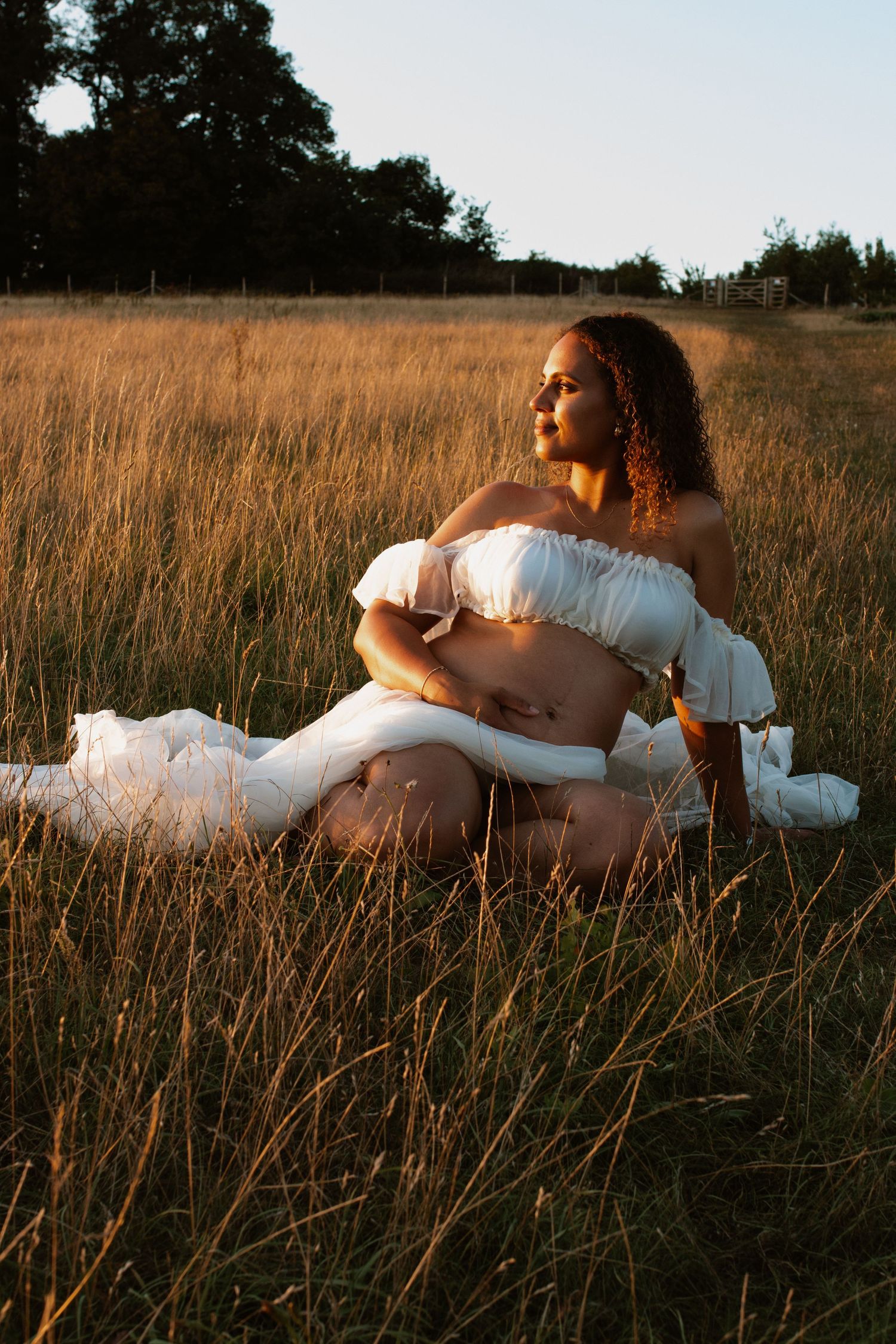 Woman in white dress sitting gracefully in tall grass during golden hour.