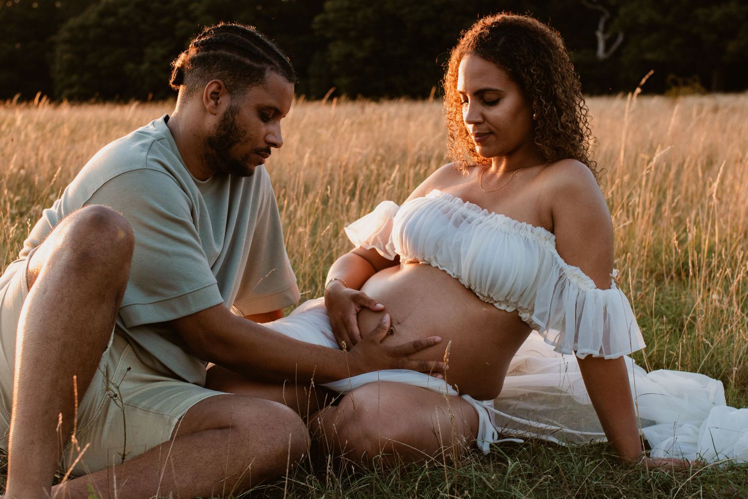 Intimate maternity photoshoot in a sun-drenched field at dusk.