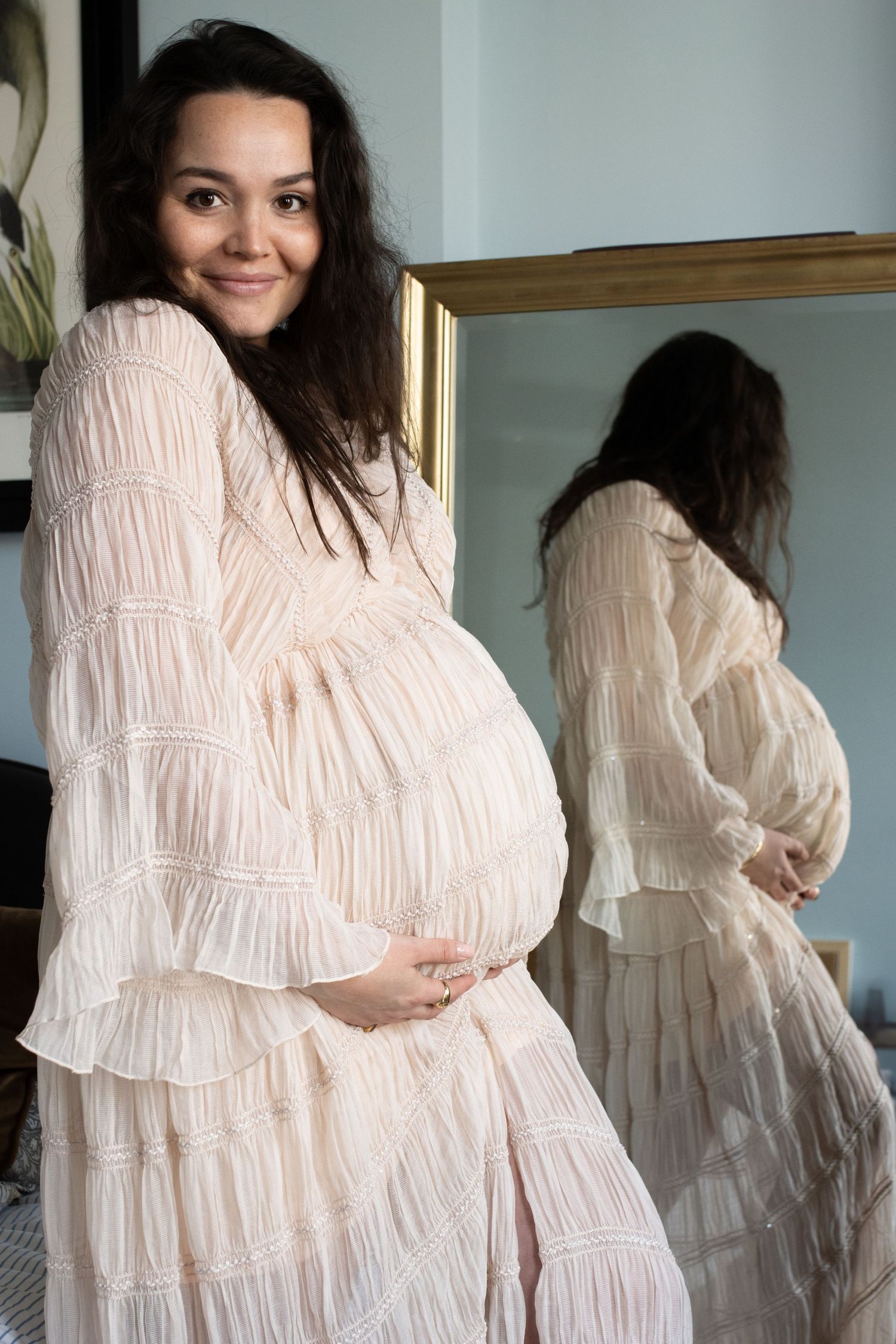 Maternity mirror portrait in ruffled cream dress showing pregnancy silhouette.