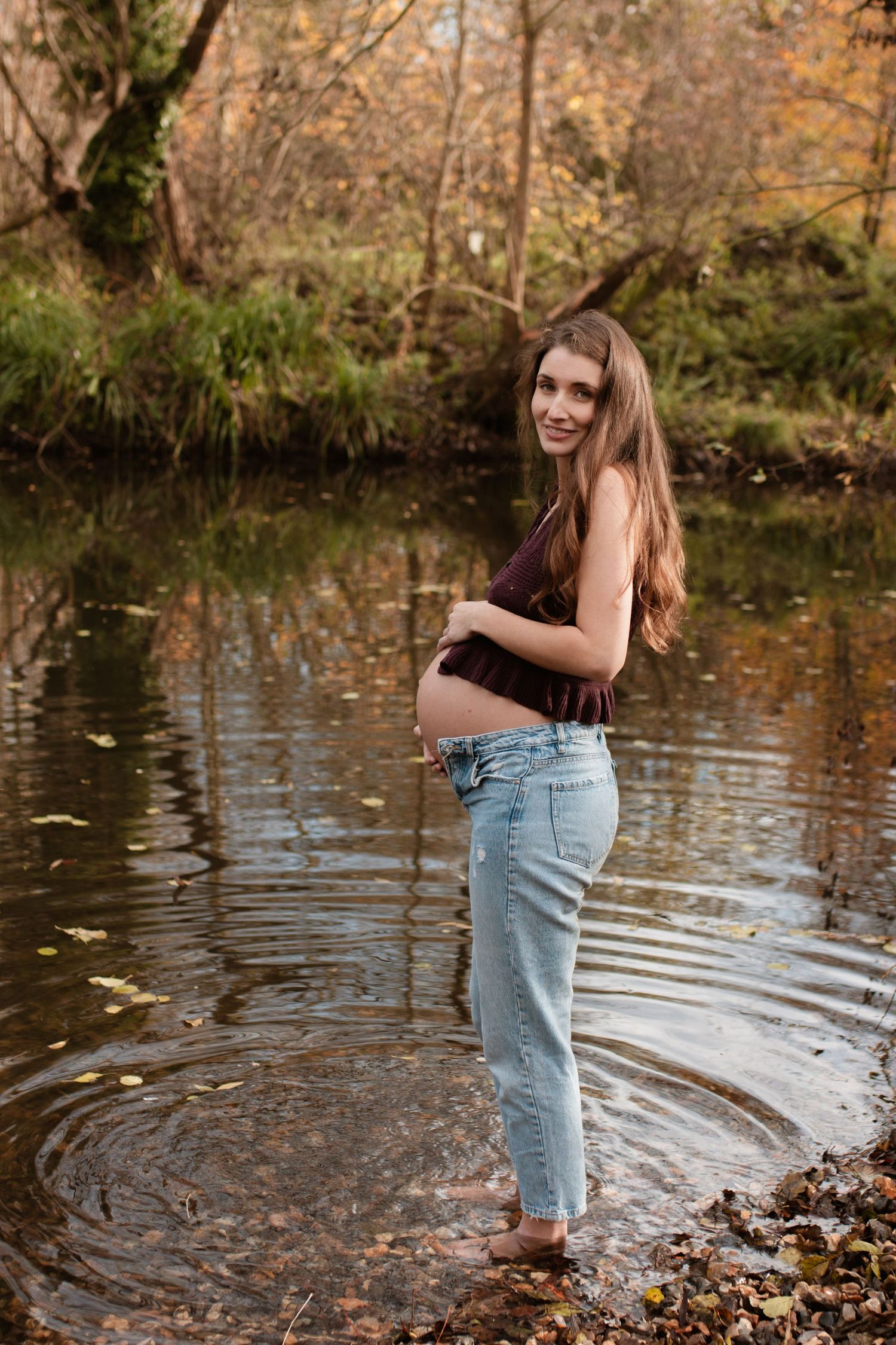 Expectant mother standing in creek during autumn maternity photoshoot.