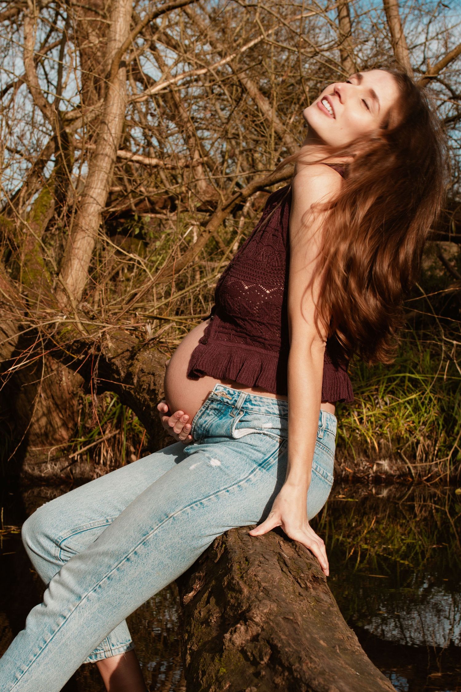 Maternity portrait in autumn setting with woman posing on fallen tree trunk.