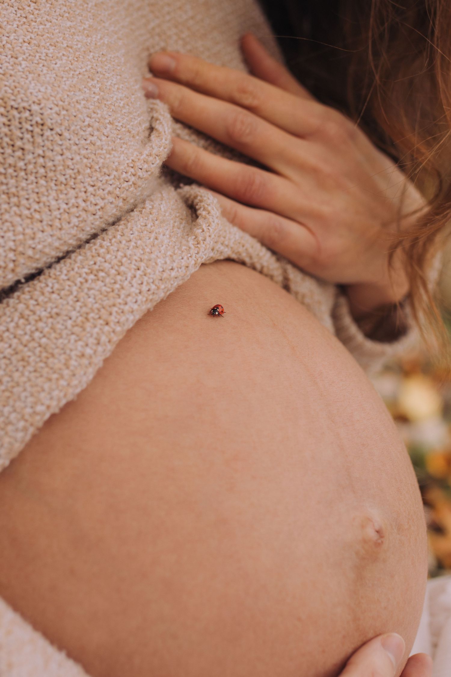 Close-up of pregnant belly with piercing against soft knit sweater.
