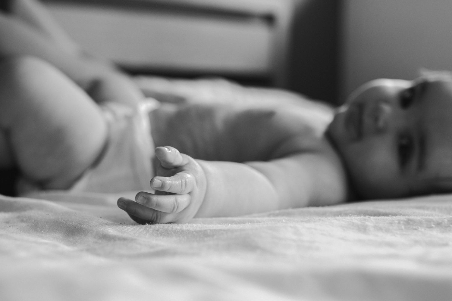 Black and white close-up of baby's hand resting on soft bedding.