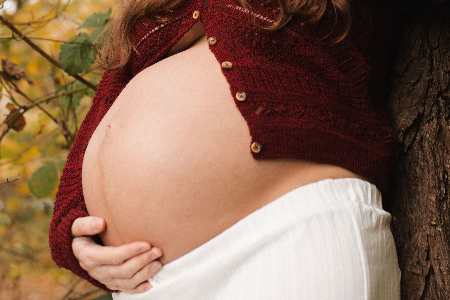 Close-up maternity photo showing a pregnant belly against burgundy and white clothing.