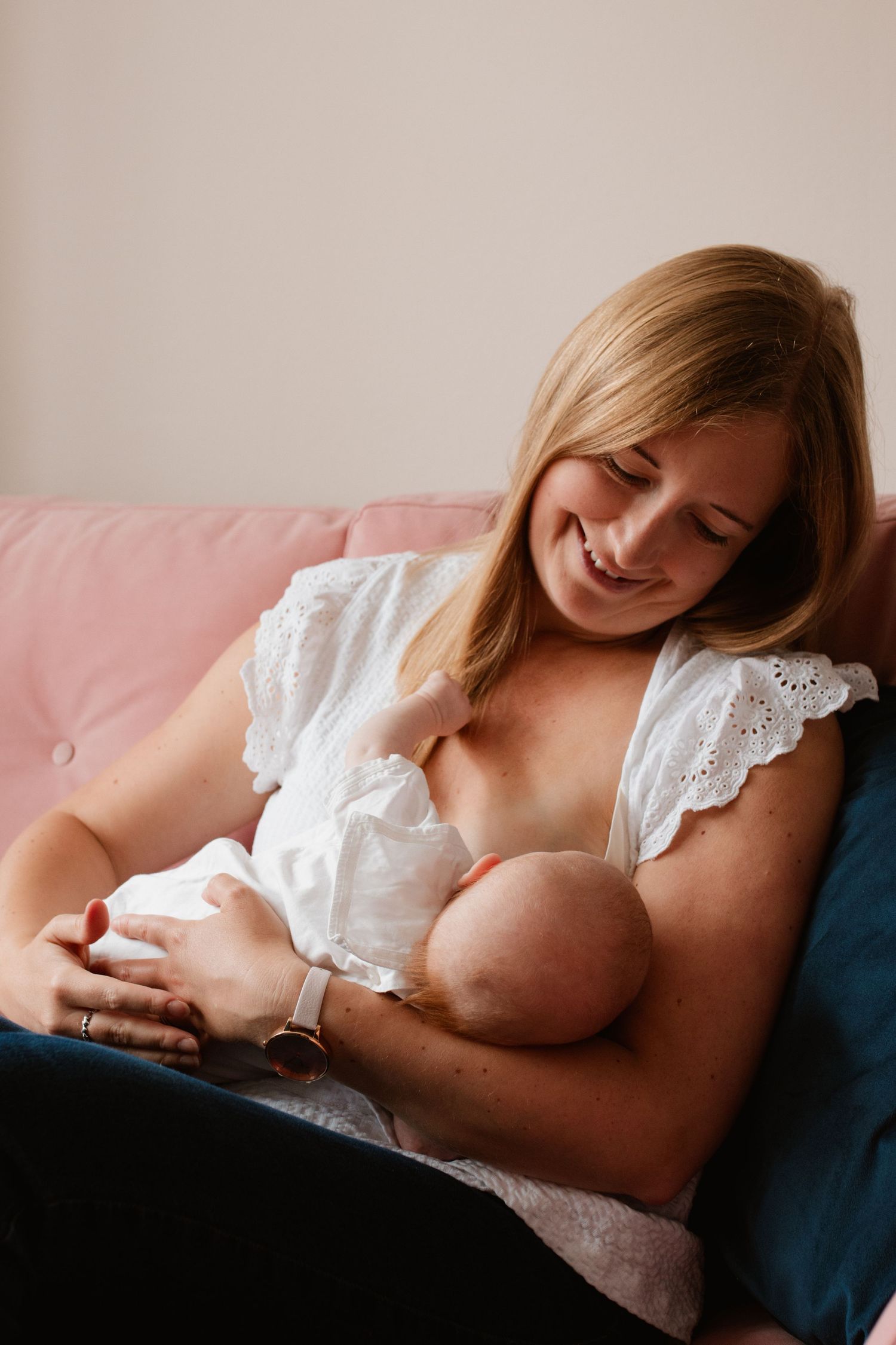 Intimate nursing moment on blue couch in soft lighting.