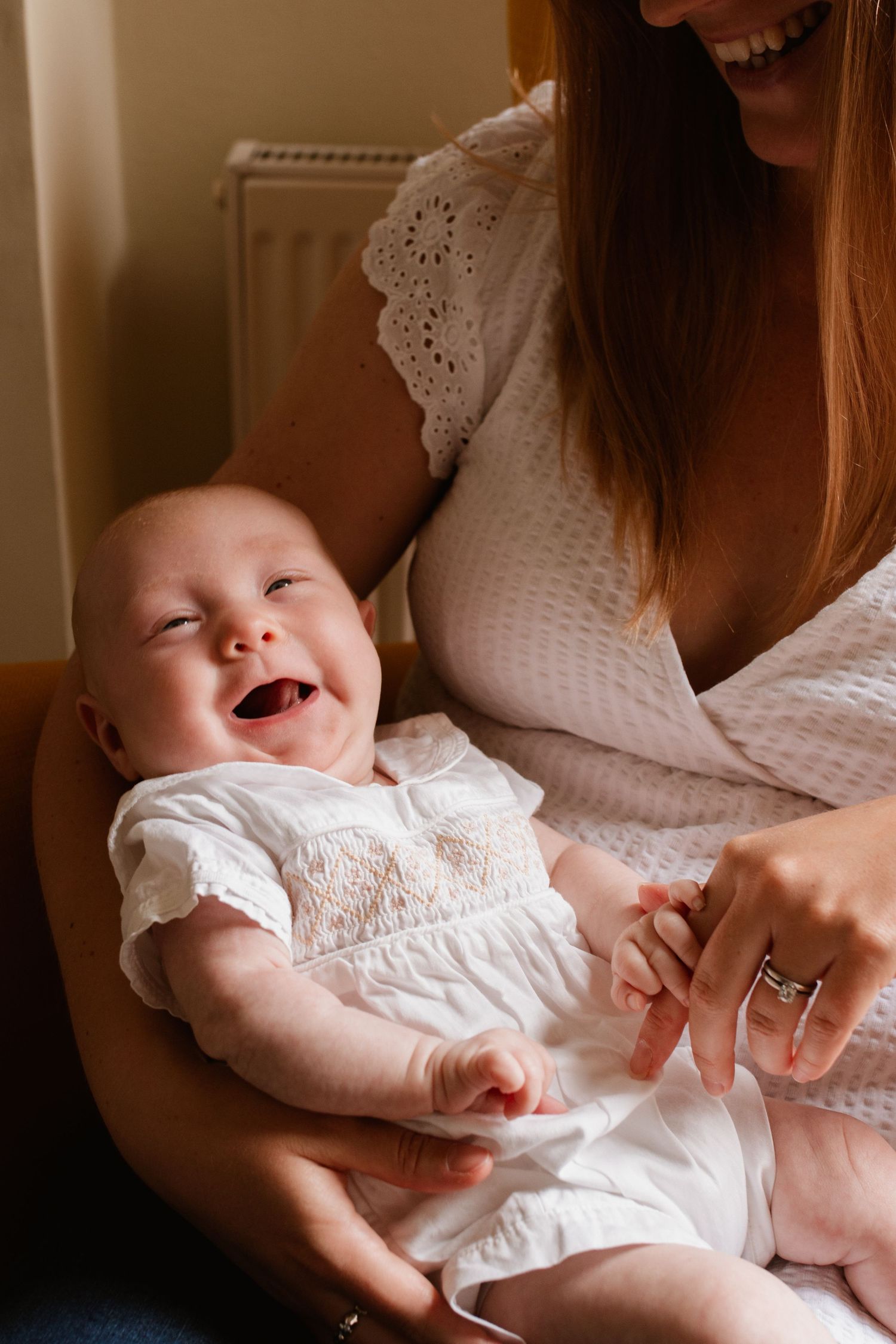 Baby in white outfit laughing while being held.