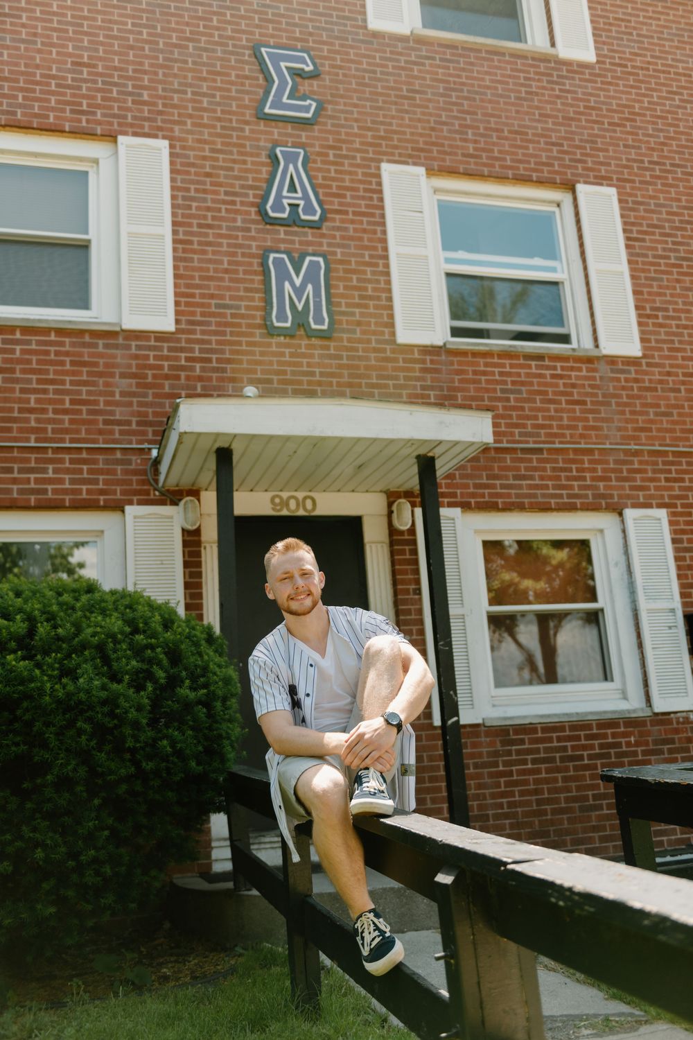 Person sitting on outdoor concrete ramp outside brick building entrance with multiple windows.