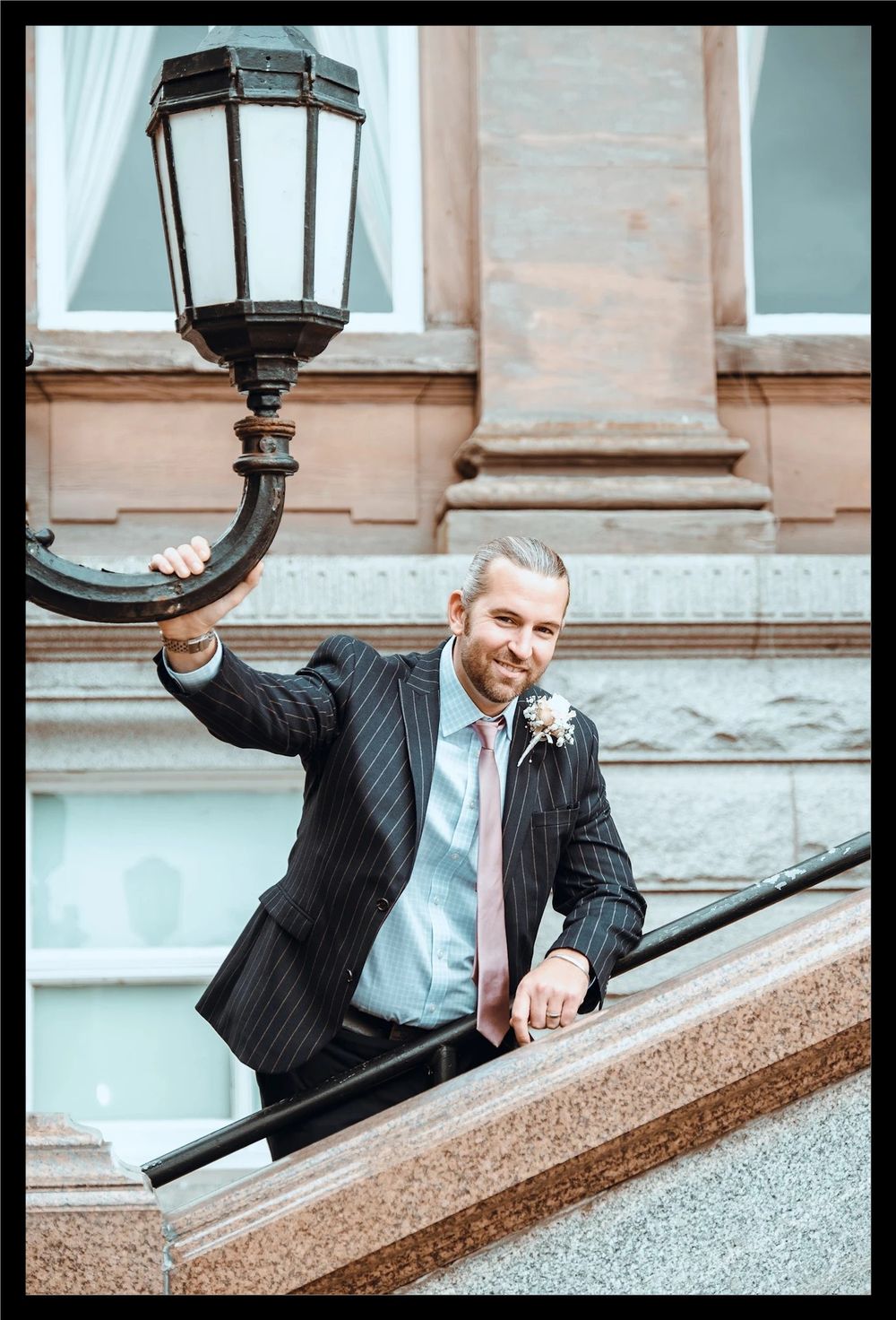 An elegant staircase with decorative streetlamp and classic architectural features frames a stylish urban scene with the groom.