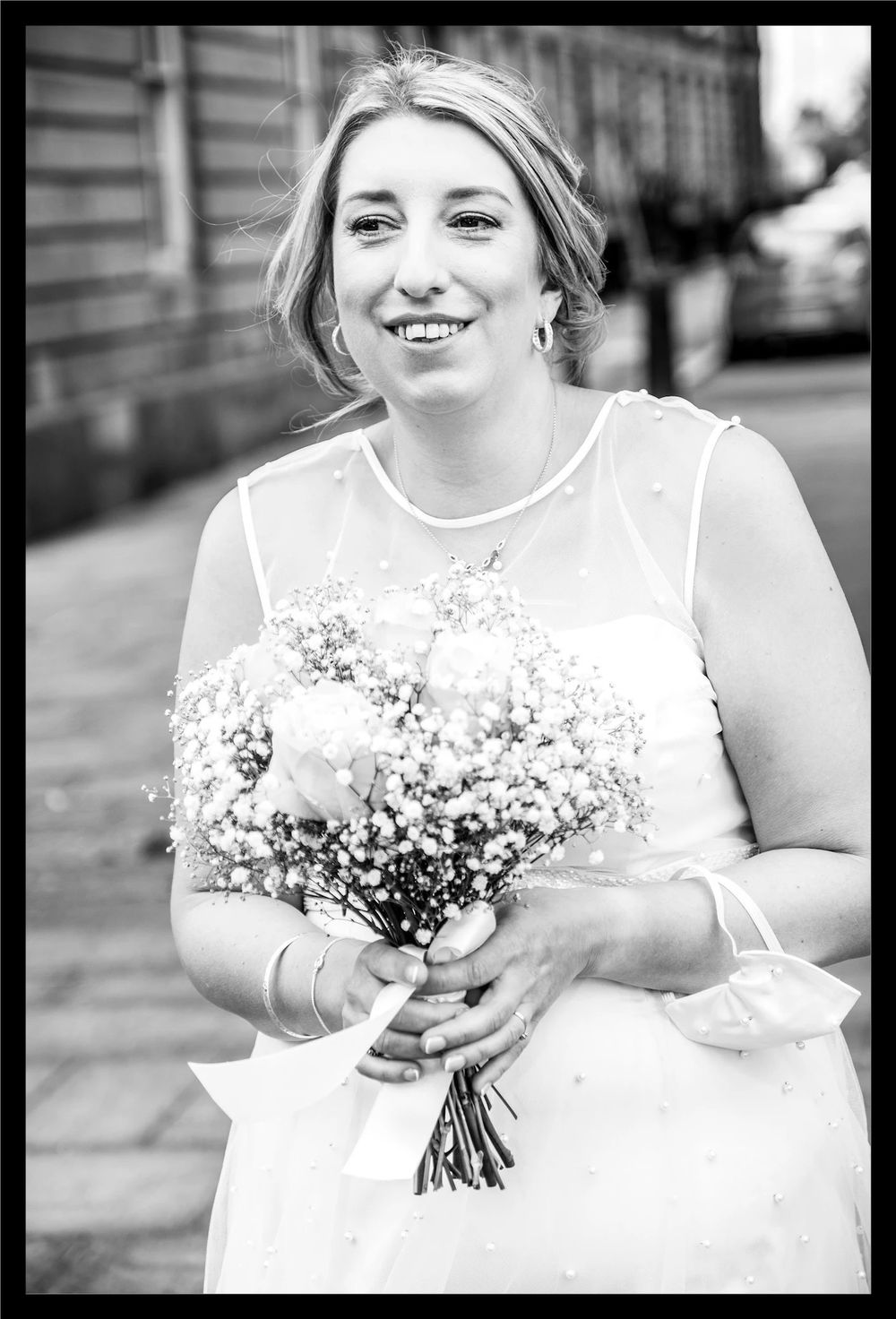 A black and white portrait of a joyful bride in a white dress holding a delicate bouquet of baby's breath flowers.