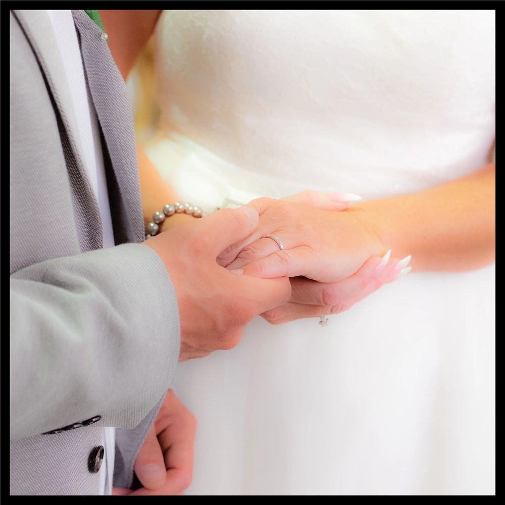 Close up of bride and groom holding hands tenderly during a wedding ceremony, with groom wearing light gray suit.
