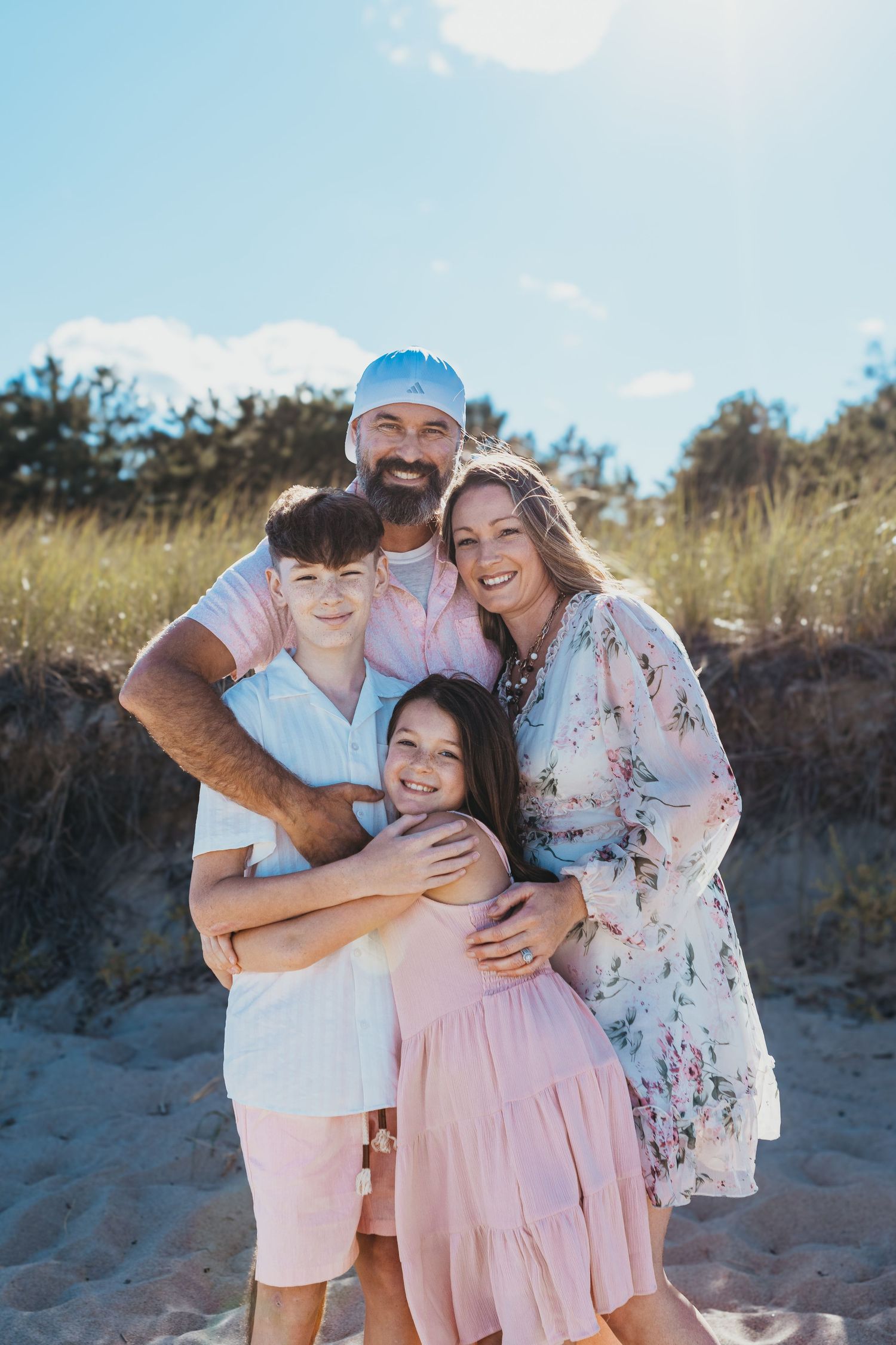 Beach family photoshoot with coordinated pastel outfits against sandy backdrop.