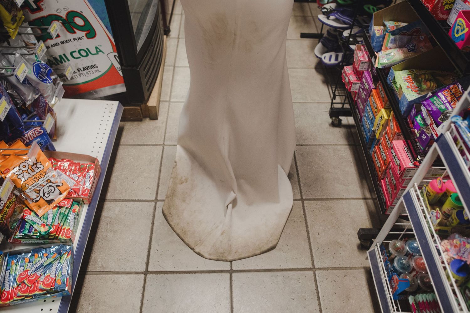 Dirty footprint marks on white tile floor in convenience store aisle between shelves of snacks and candy.