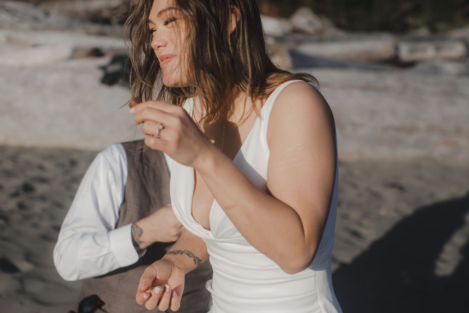 A person in a white dress sits on a beach while the breeze blows through their hair in soft sunlight.