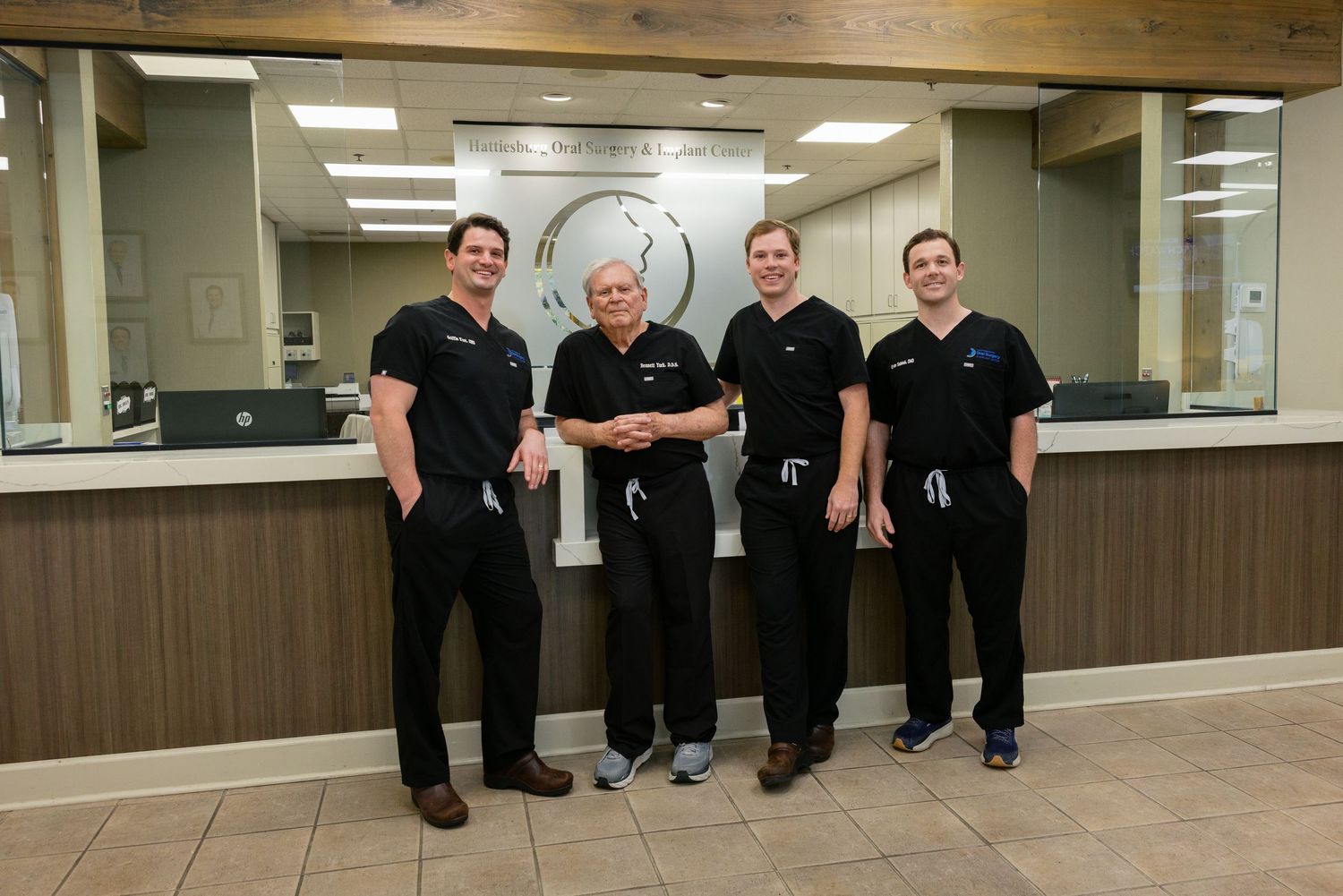 Healthcare workers in black scrubs sit together along a hallway wall in a medical facility.