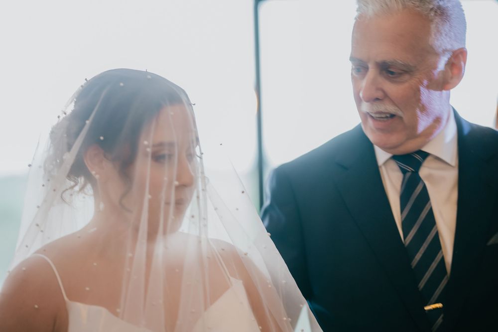A wedding scene showing an elegant bride wearing a veil standing next to someone wearing a dark suit with striped tie.