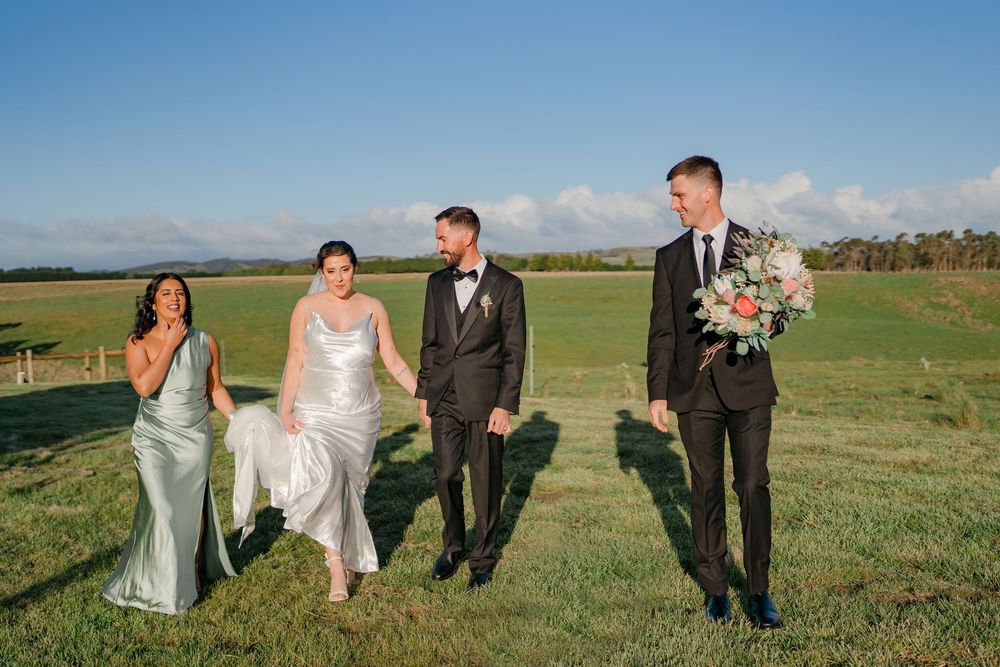 Wedding party walks together through scenic green rolling hills on a sunny day with blue skies.