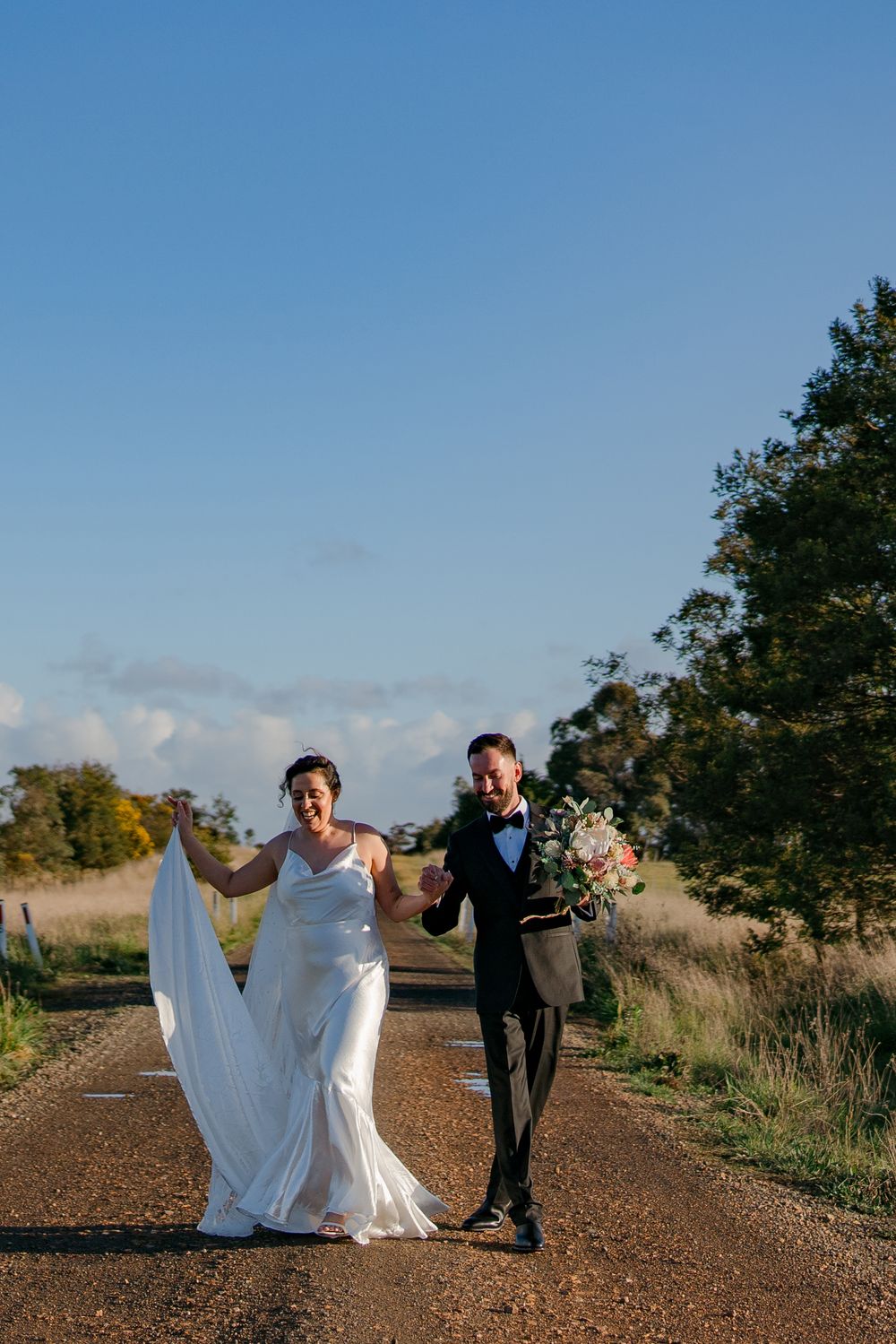 Three artistic wedding photos taken on a country dirt road with people walking together against a blue sky backdrop.