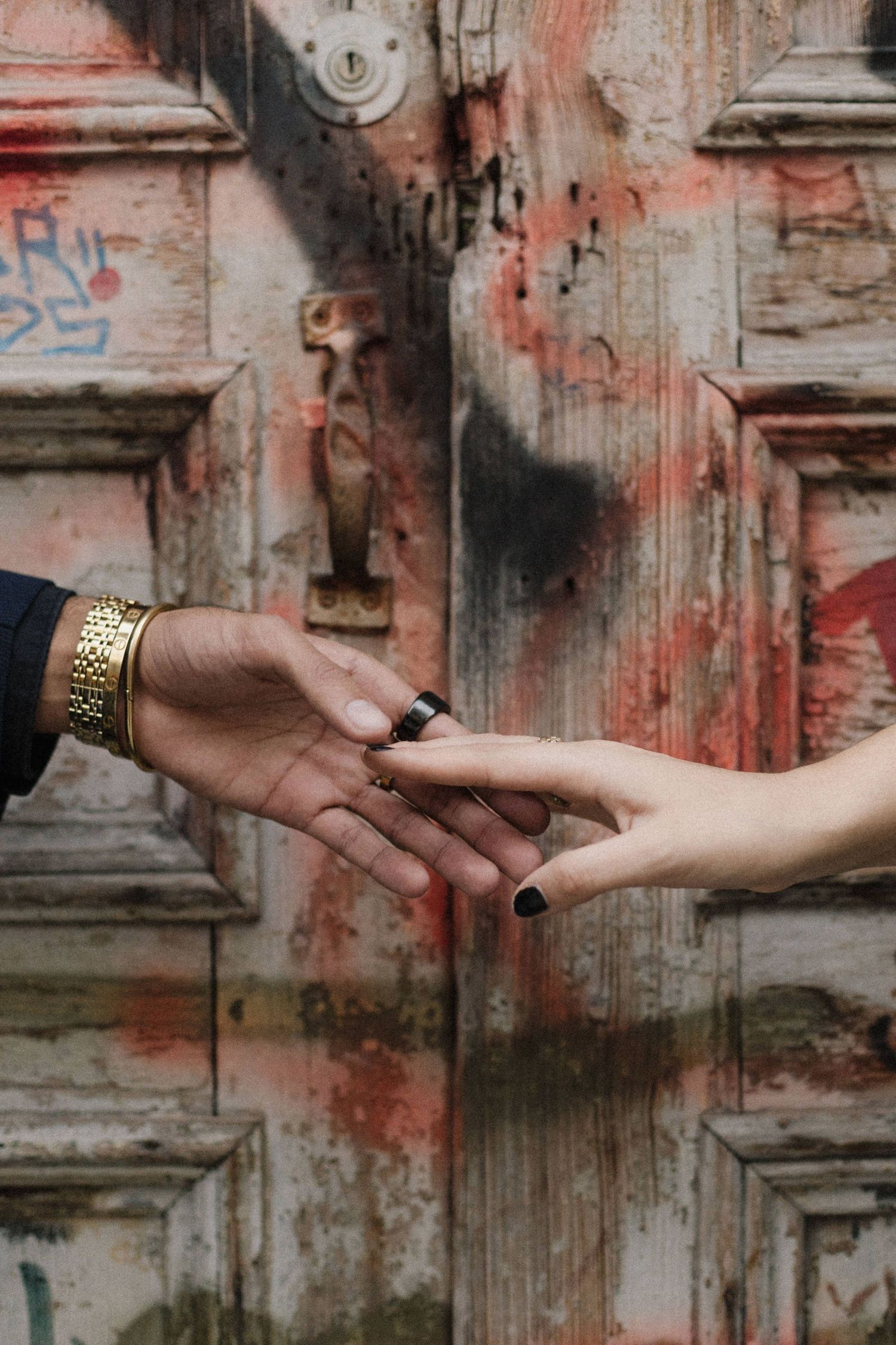 Close-up shot of two hands reaching towards each other against a weathered red wall with graffiti.