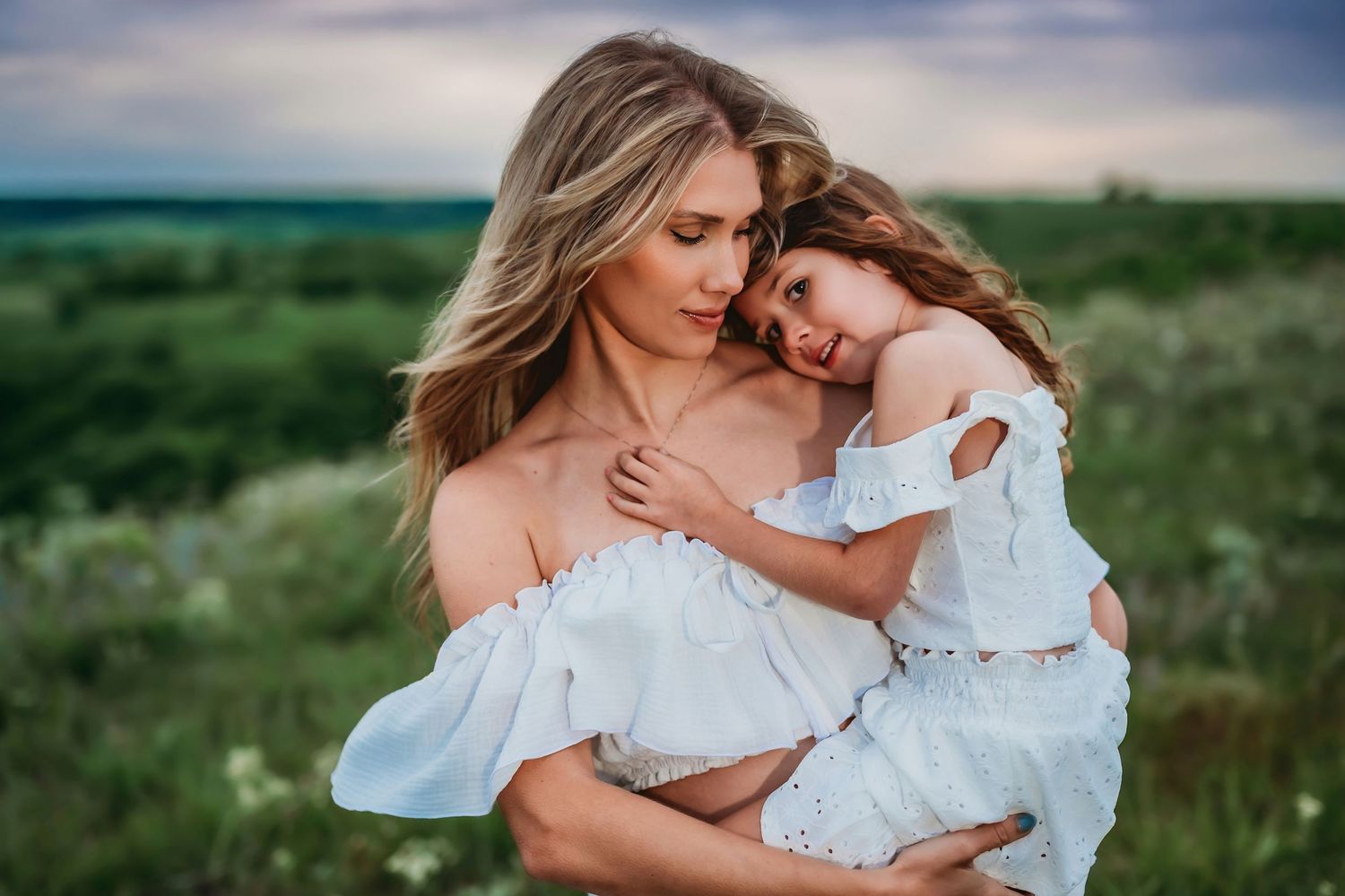 Family posing in white outfits against a lush green field during golden hour outdoor photo session.