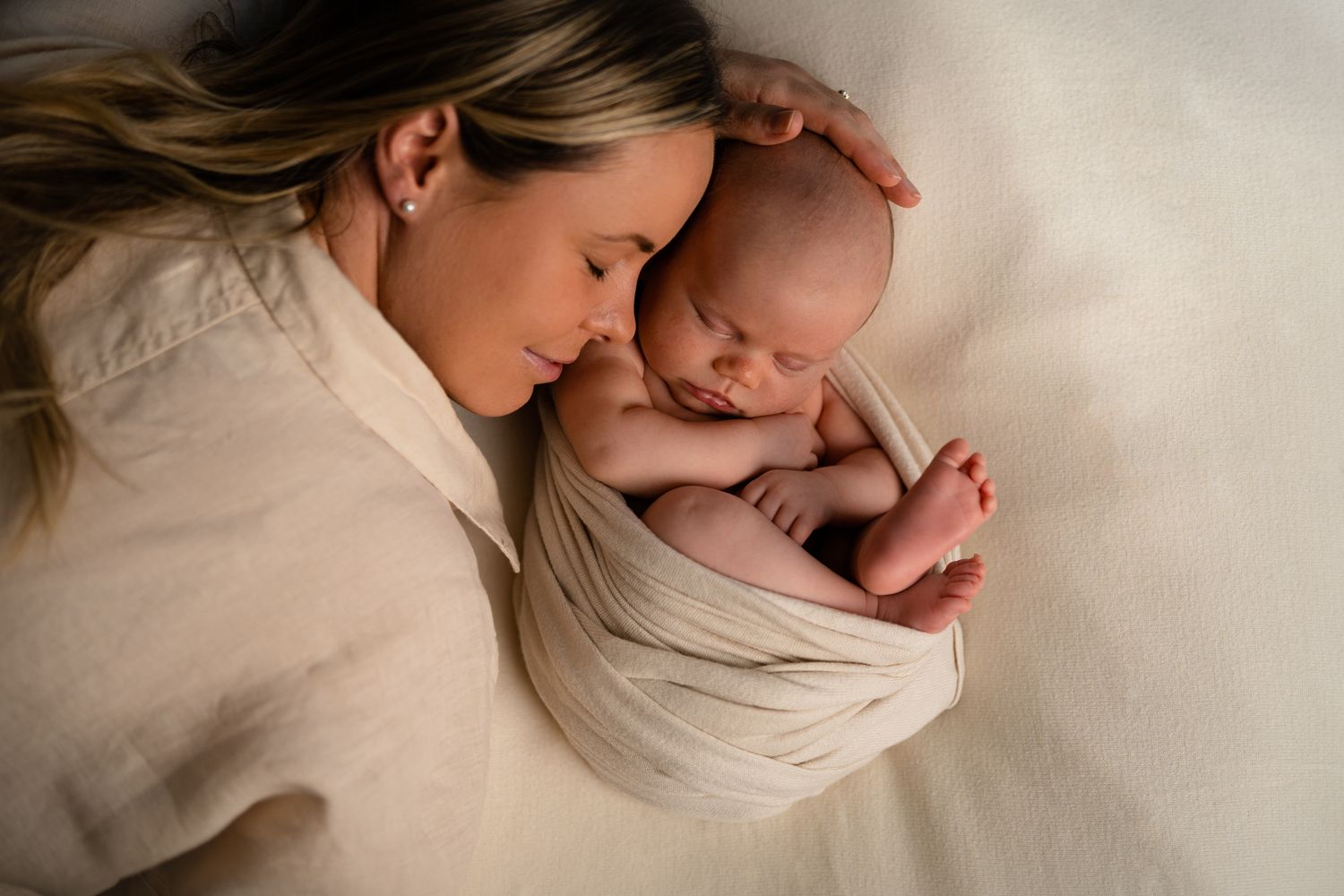 A tender moment between a parent and newborn baby wrapped in soft beige fabric during a professional studio photo session.