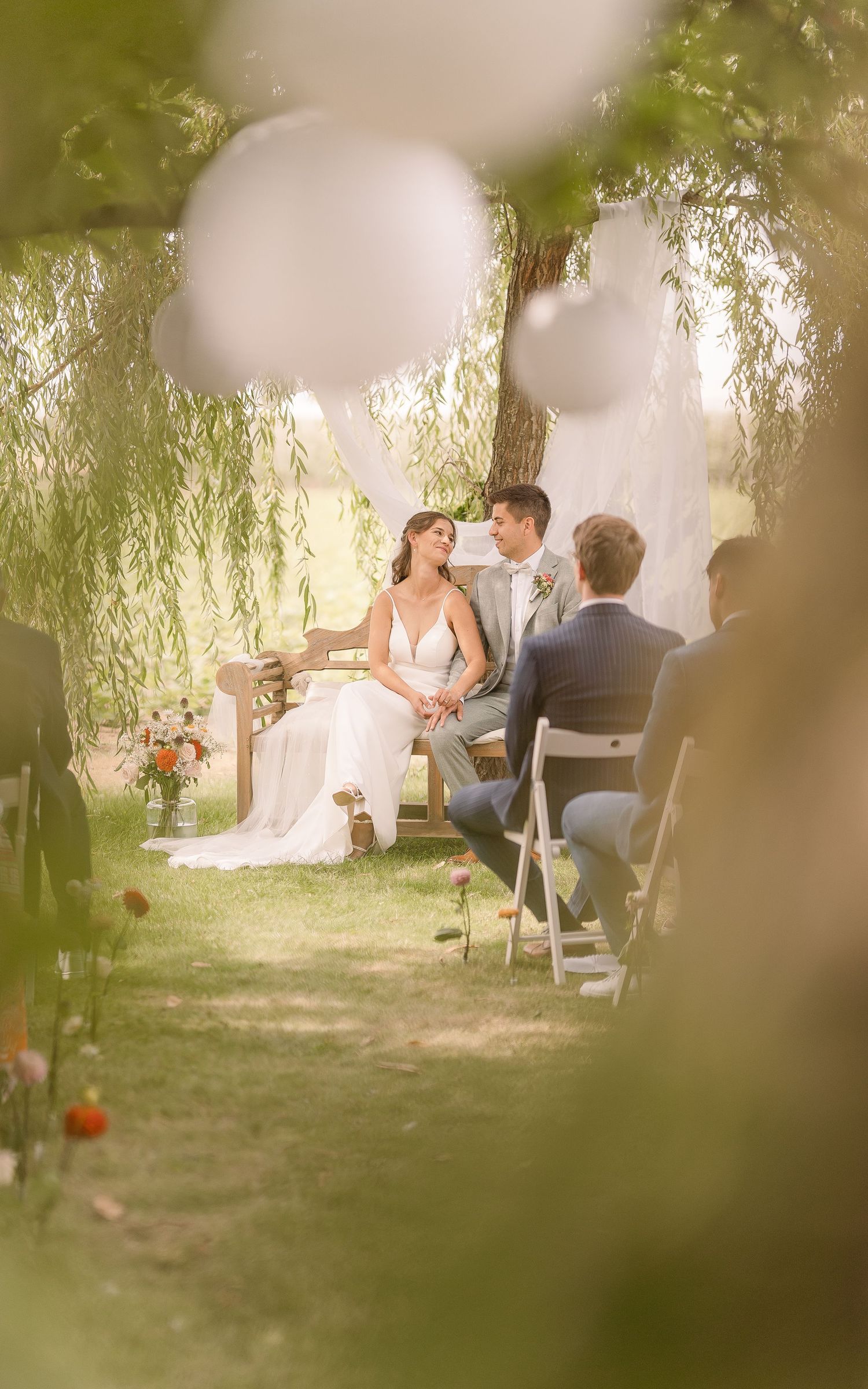 Wedding ceremony scene through white balloon decorations and willow branches.
