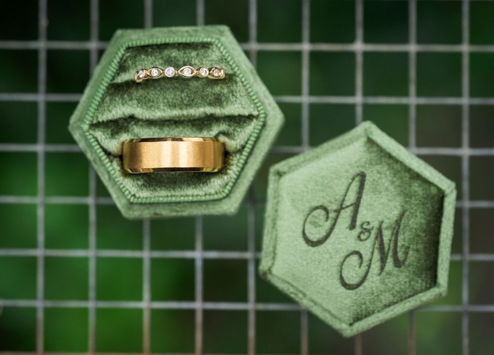 Elegant wedding rings and monogrammed decor items arranged on a green background with hexagonal shapes.