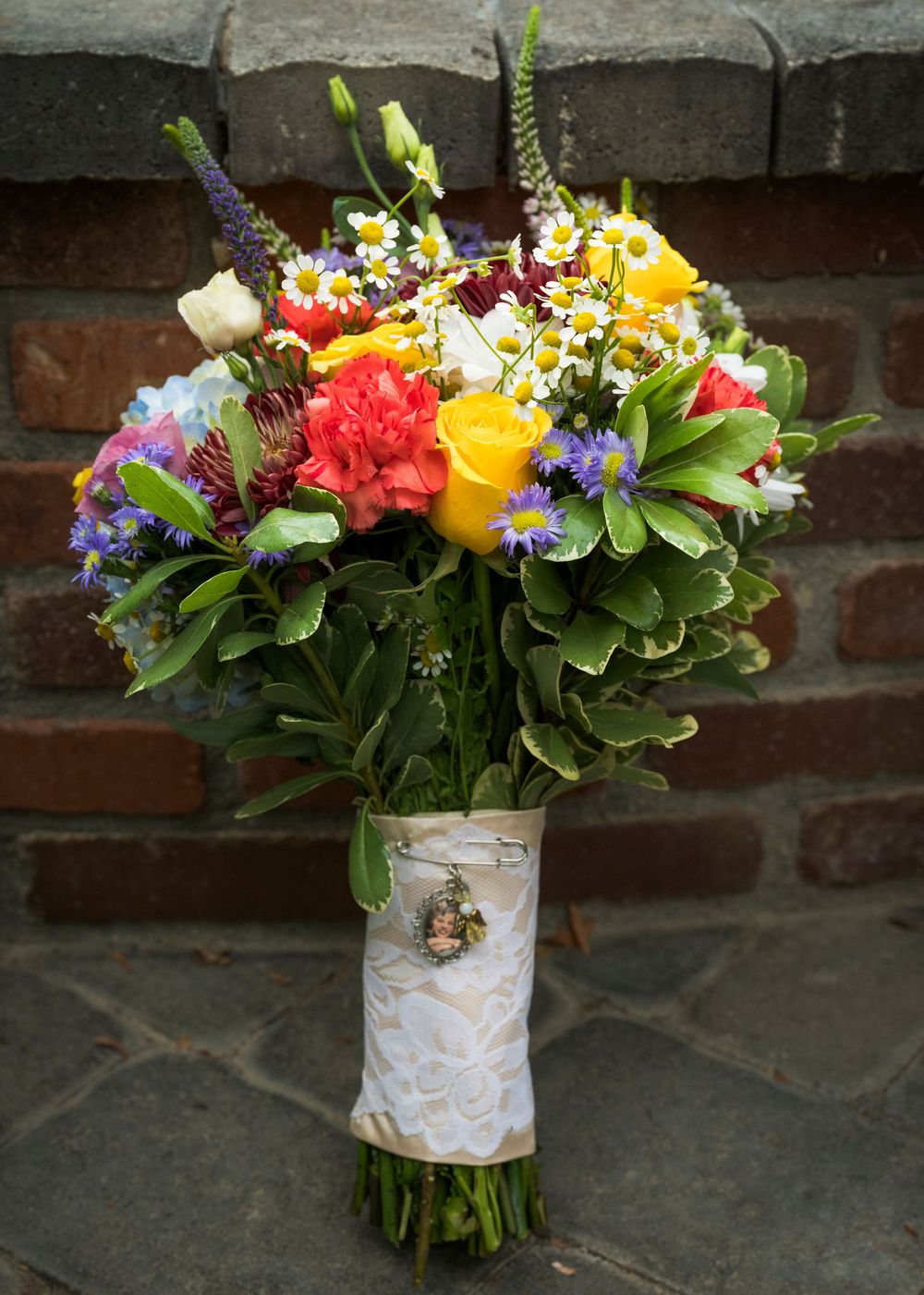Colorful wedding bouquets wrapped in lace ribbon displayed against a rustic brick wall.