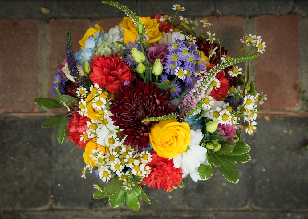 Vibrant floral arrangement with red, yellow, and white flowers against a rustic brick wall background.