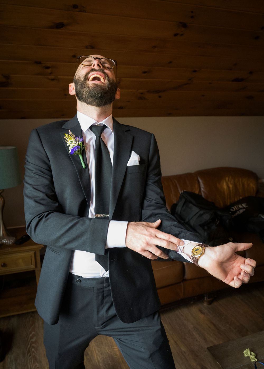 Wedding party members in formal attire share candid laughing moments in rustic wooden venue.