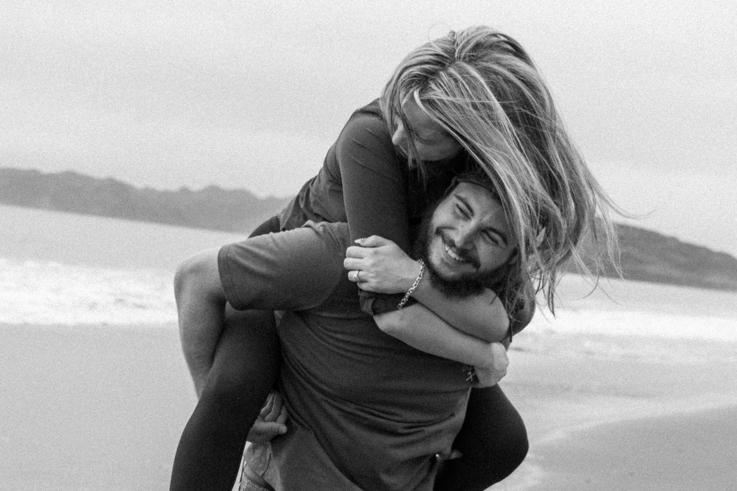 A romantic proposal unfolds along a scenic coastal cliff with mountains and ocean views at golden hour.