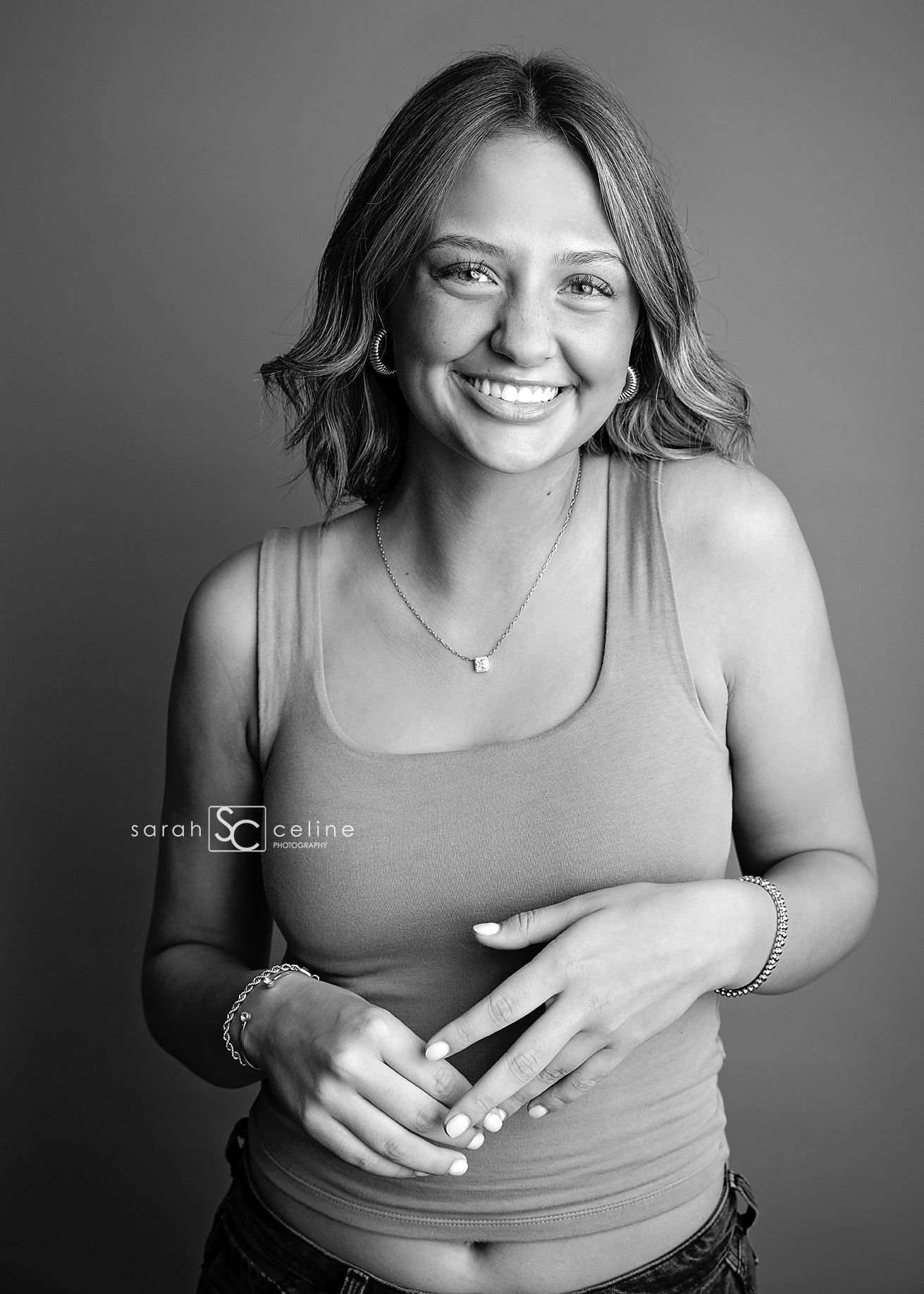 Black and white portrait showing a bright smile and casual tank top in a professional studio setting.
