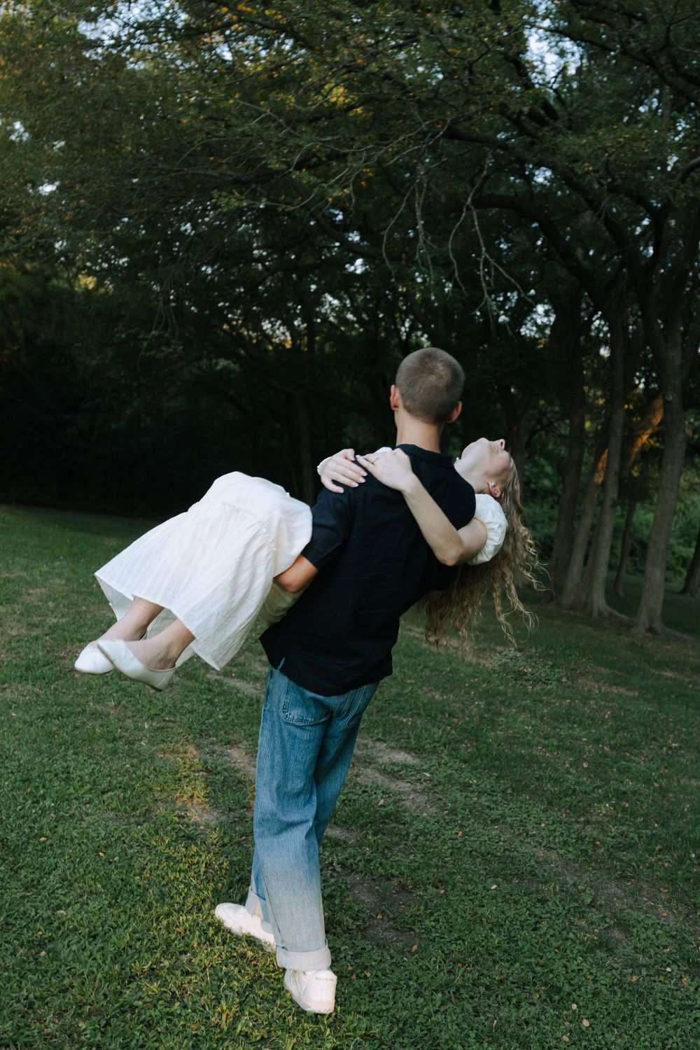 A couple performs a playful dance move on a grassy hillside at sunset.