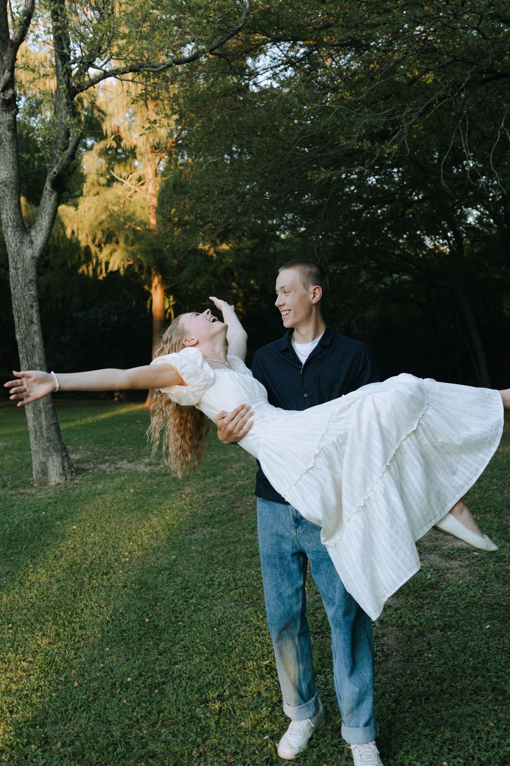Two people dance together on a grassy slope with trees in the background.