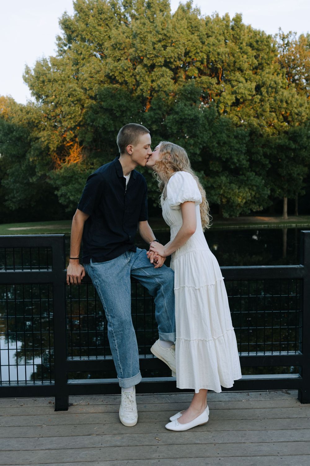 Couple shares tender moment on wooden deck overlooking water during sunset.