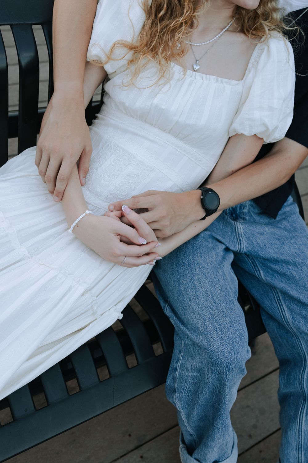 Close-up of couple sitting on bench, showing white dress and blue jeans details.