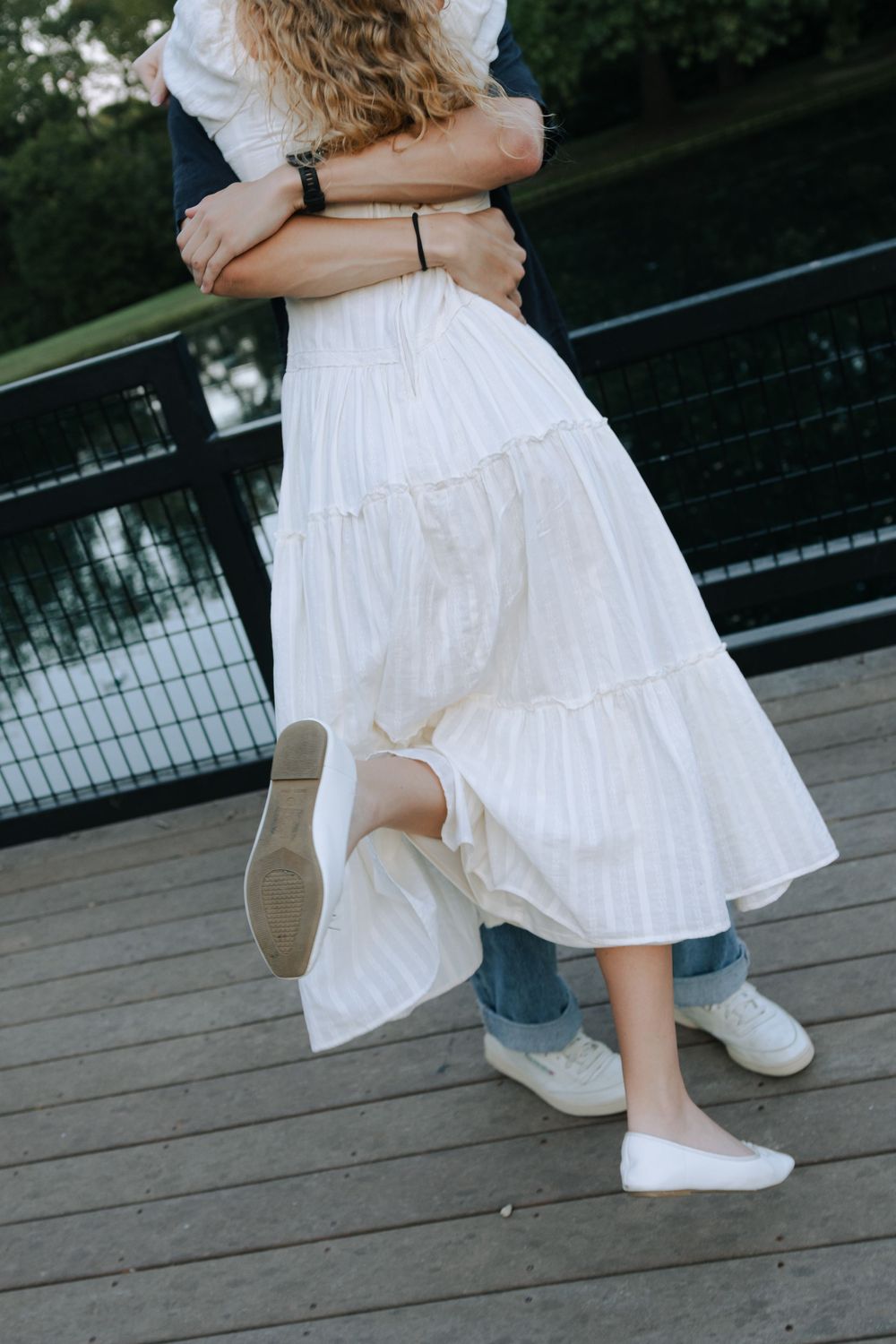 Close-up of dancing feet on a wooden deck, showing a white dress and casual denim.
