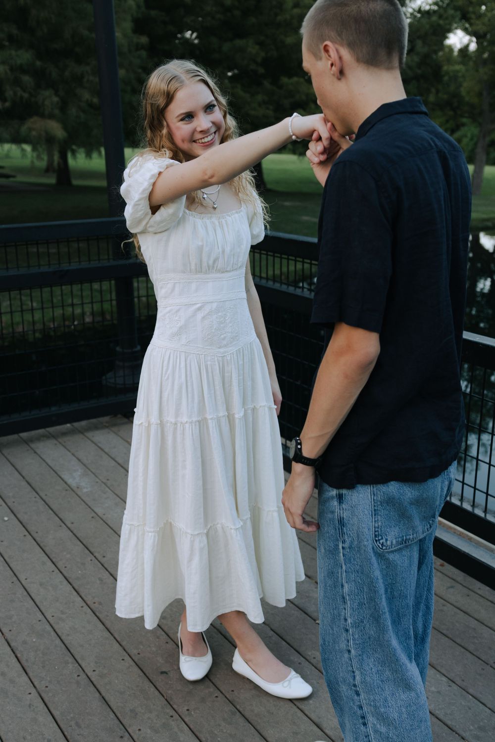 Couple in white dress and casual wear dancing together on wooden boardwalk near water.