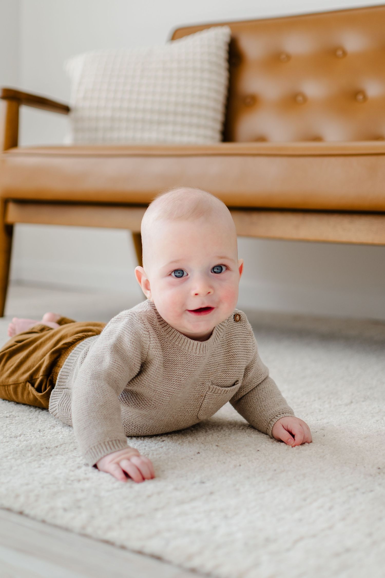 Six sequential photos show a baby laying on a white carpet wearing a beige sweater, showcasing different playful poses.