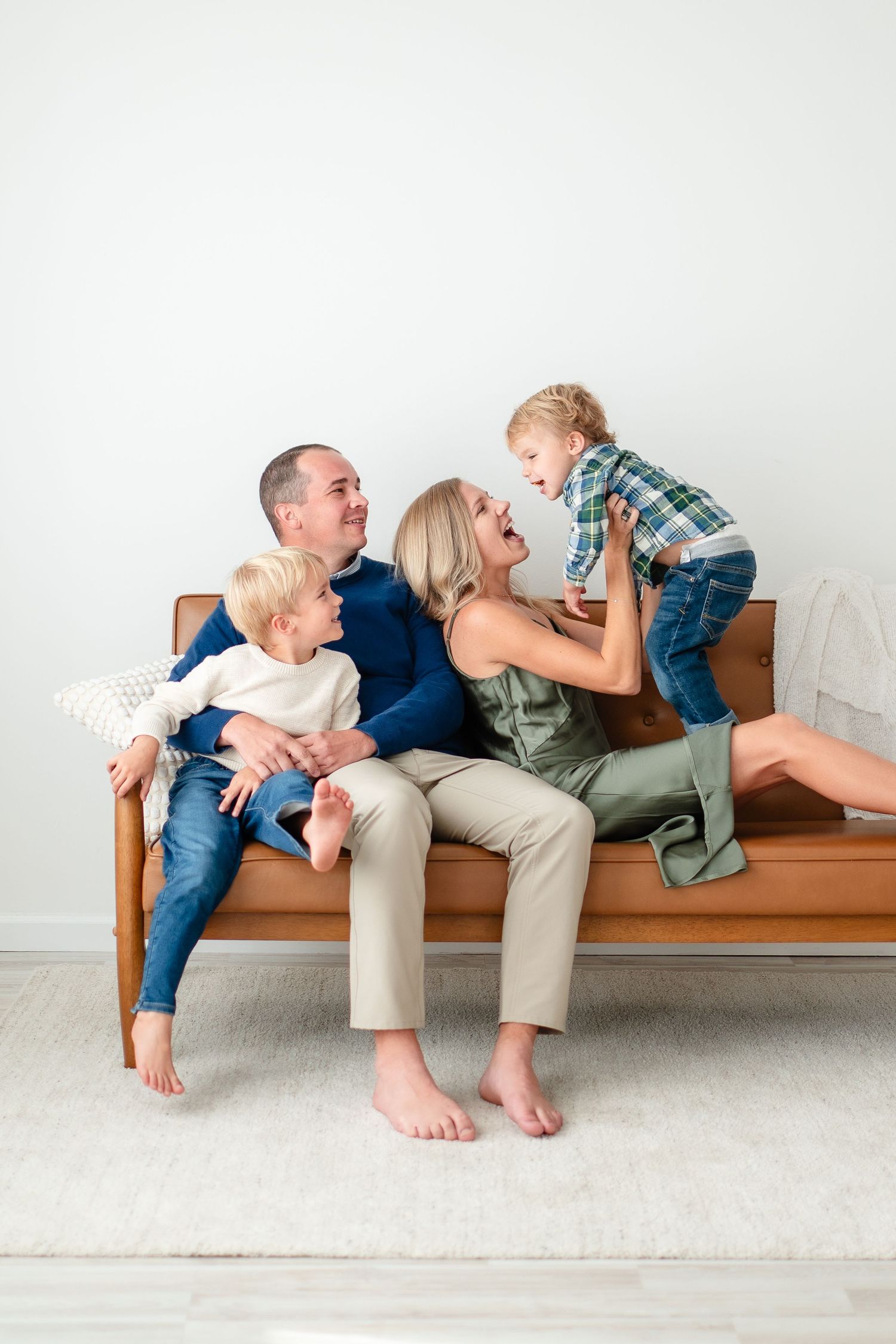 Happy family enjoying playful moment together while sitting on a tan wooden bench against white wall.